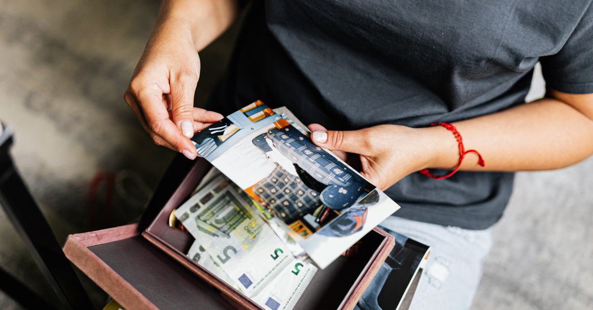A woman holding photographs over a box with euro notes indoors.